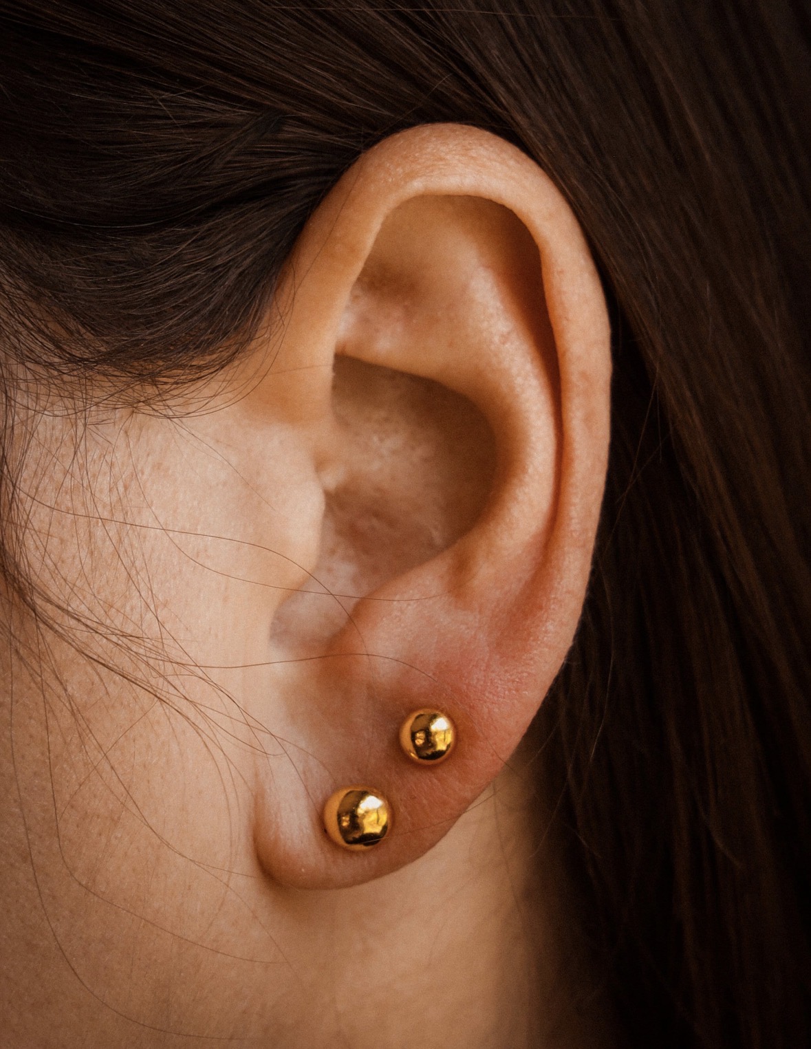 Close-up of 4mm and 5mm 24K gold ball earrings on a customer
